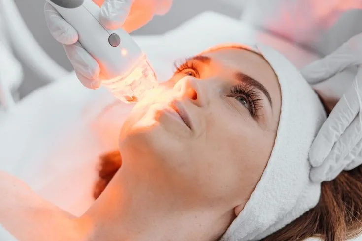 Bác sĩ dùng thiết bị chiếu ánh sáng lên vùng mặt của người được chăm sóc da