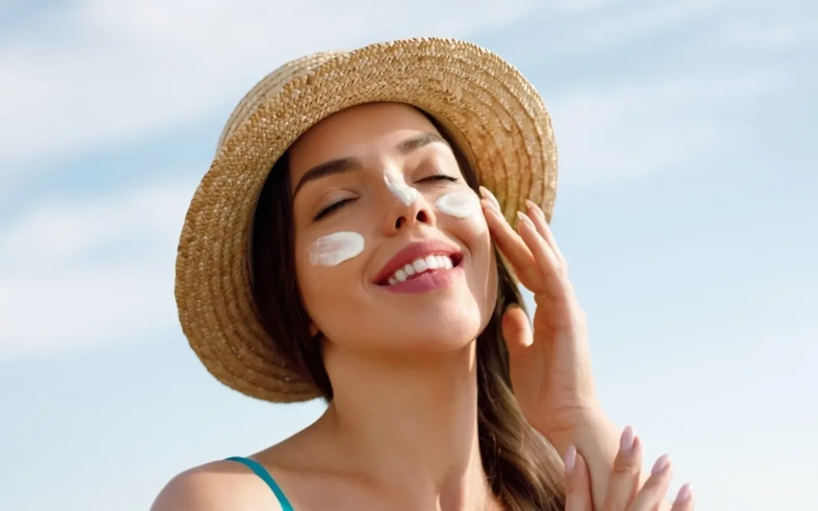 Người phụ nữ đội mũ rộng vành, đang thoả kem chống nắng lên mặt